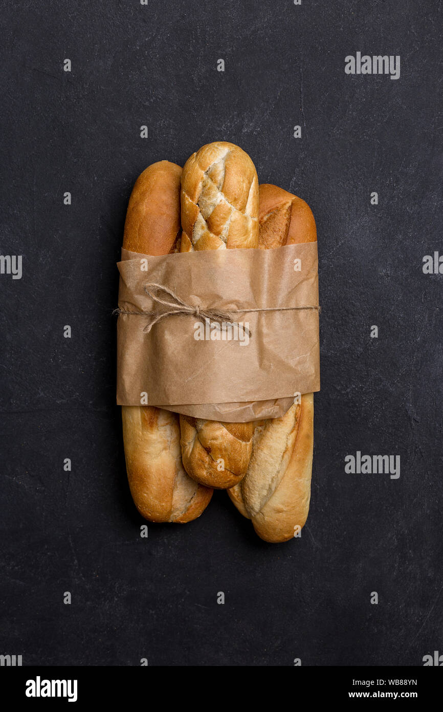 Tree loafs of bread in craft paper at black background. Concept of banner for market Stock Photo