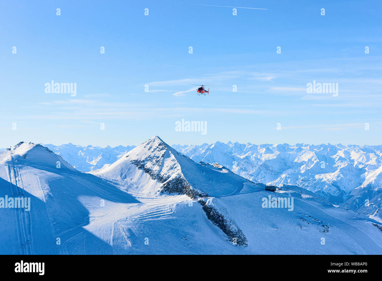 Flying Red Helicopter over Hintertux Glacier ski resort in Zillertal in Tyrol in Austria in winter in Alps. Chopper and Alpine mountains with snow. Ai Stock Photo
