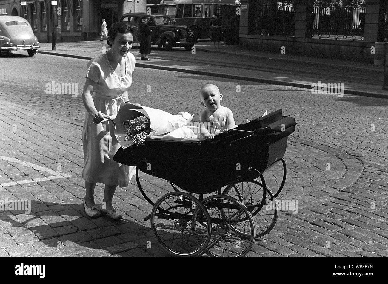 Mother with child in the 1950s. She walks in the street pushing the stroller in front of her with her baby in it. Sweden 1953. Kristoffersson Stock Photo