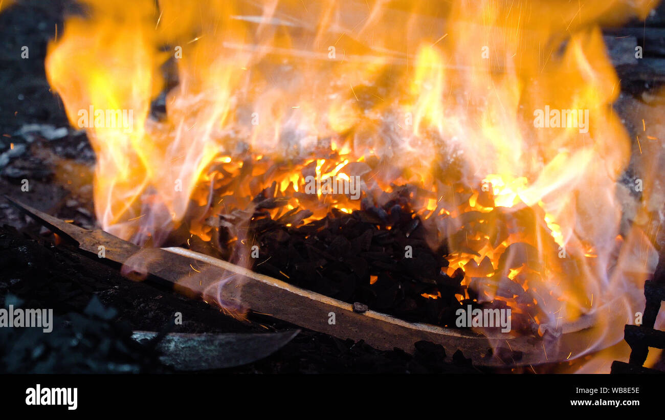 Blacksmith furnace with a hot iron, burning embers, sparks. Machete, a knife in a blacksmith's furnace. Stock Photo
