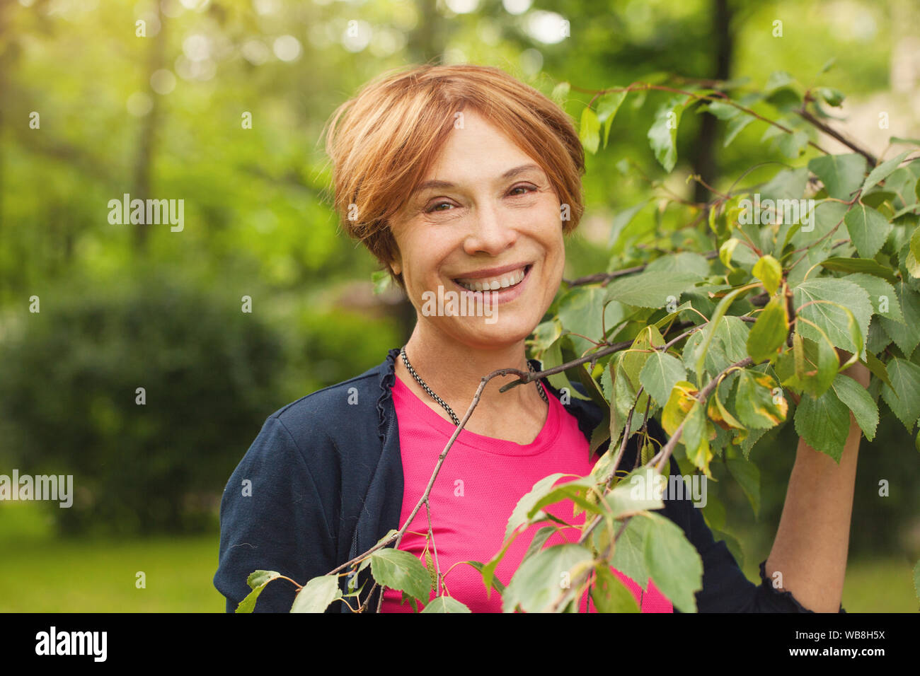Healthy mature woman having fun with green leaves outdoor. Beautiful model 60 years old Stock Photo