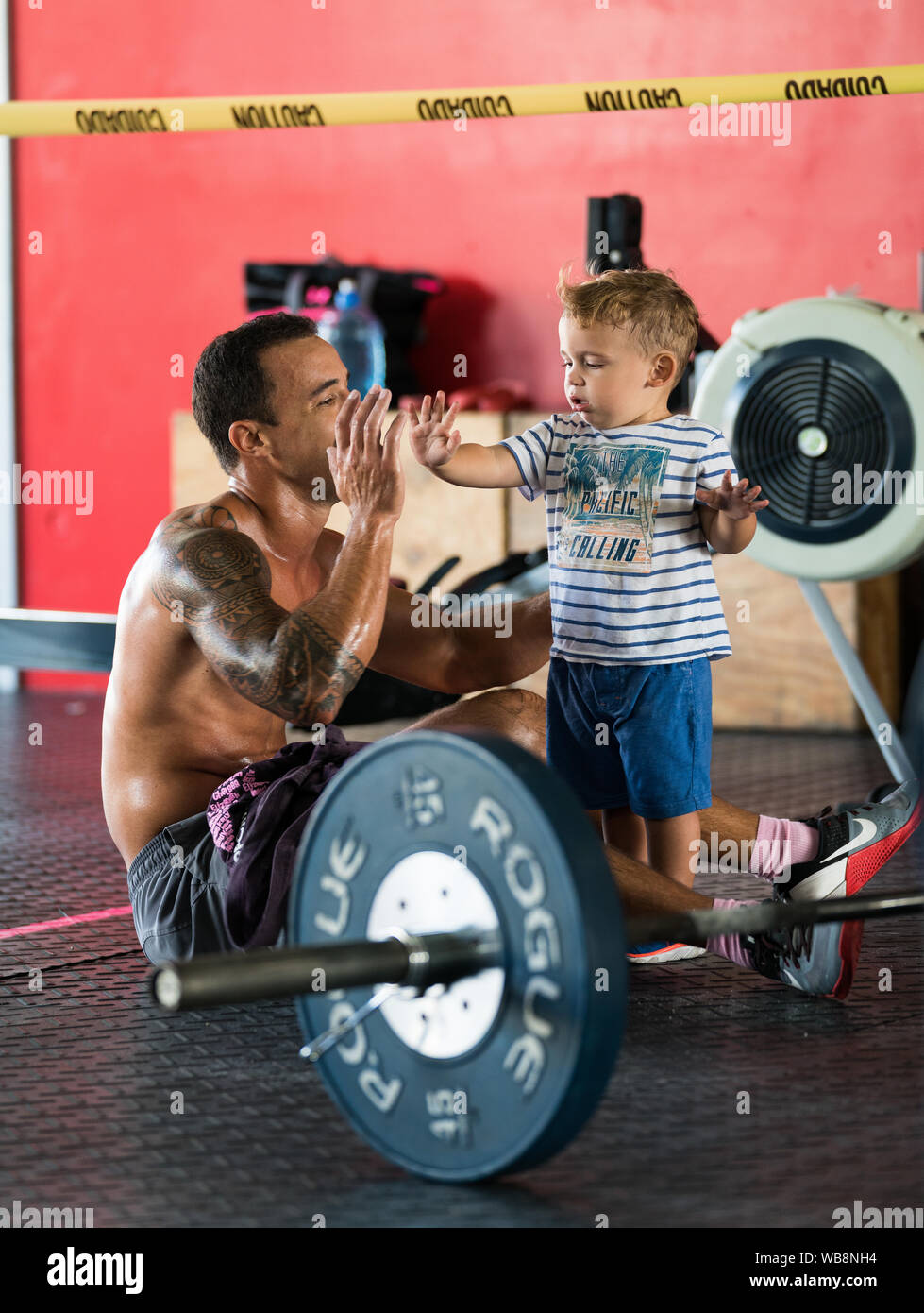 A mixed race male athlete gives a high five to his mixed race child after a weightlifting competition in the gym Stock Photo