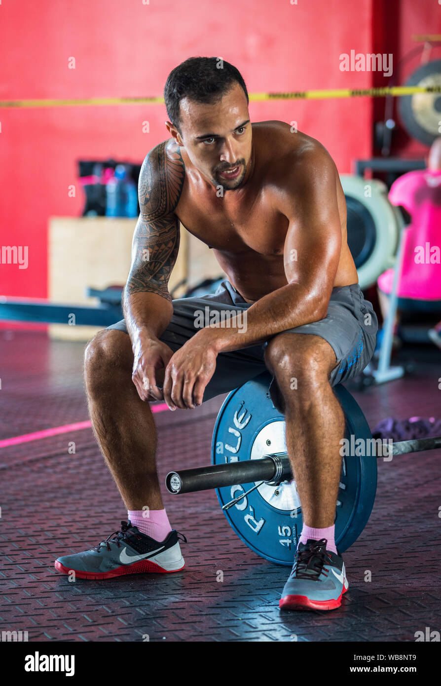 A mixed race male athlete is resting on his barbell after a weightlifting competition in the gym