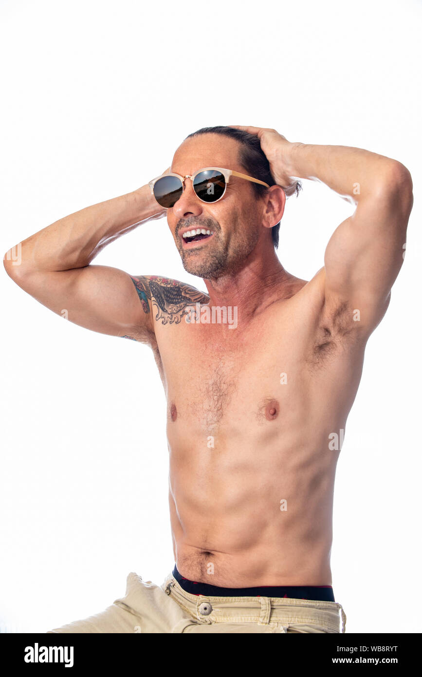 Healthy, shirless, muscular, middle aged man smiling while feeling handsome wearing reflective aviator sunglasses in high key background. Stock Photo