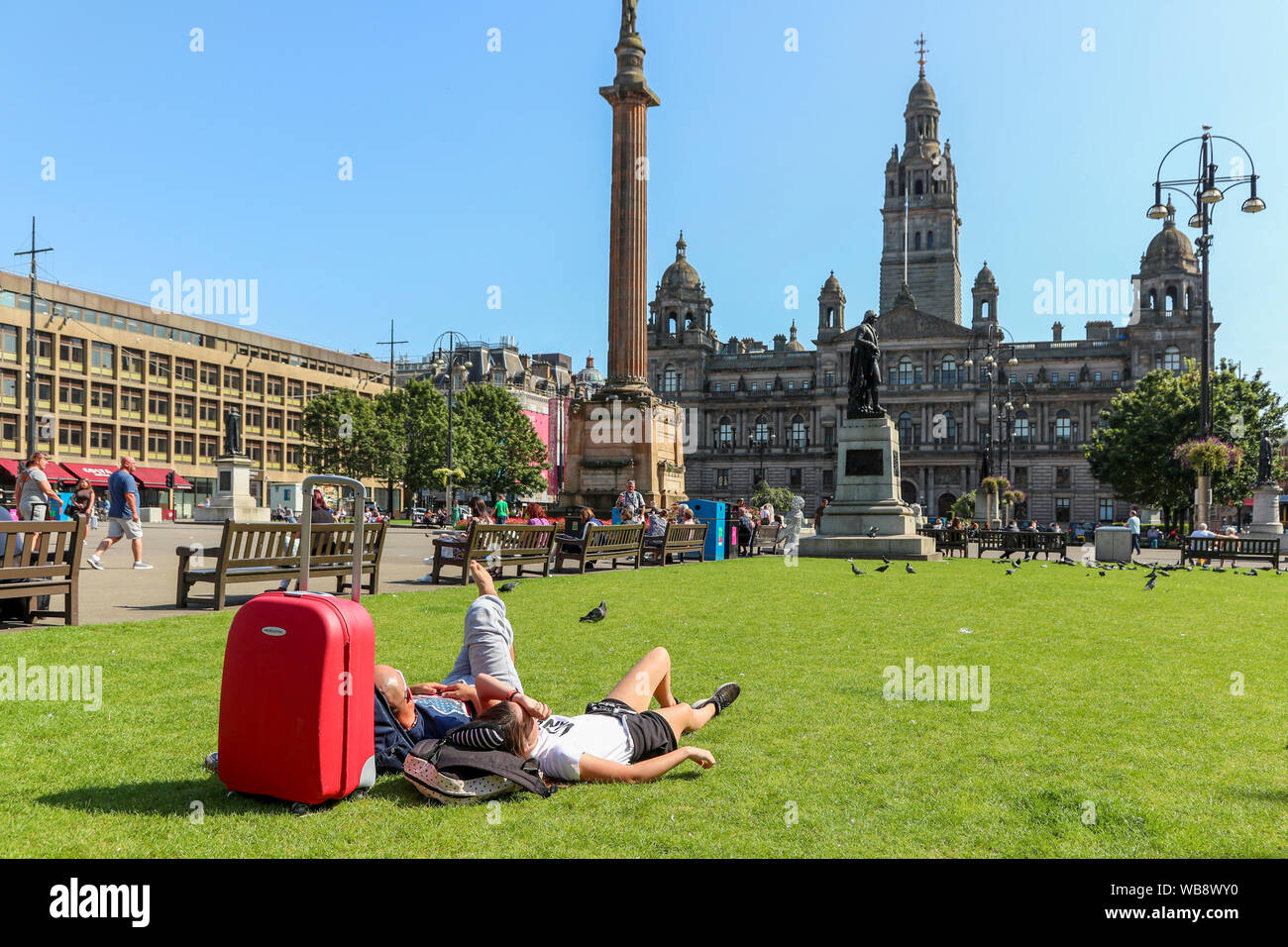 Glasgow, Scotland, UK. 25 August 2019. As temperatures soar to over 26C in Glasgow after days of rain and cold wind, people flock to the city's open spaces of George Square and the Botanic Gardens to take advantage of late summer sun on this August Bank Holiday, to top up their tans and relax. Credit: Findlay/Alamy Live News Stock Photo