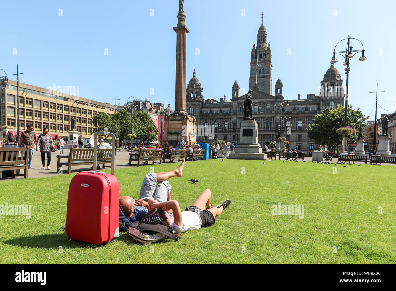 Glasgow, Scotland, UK. 25 August 2019. As temperatures soar to over 26C in Glasgow after days of rain and cold wind, people flock to the city's open spaces of George Square and the Botanic Gardens to take advantage of late summer sun on this August Bank Holiday, to top up their tans and relax. Credit: Findlay/Alamy Live News Stock Photo