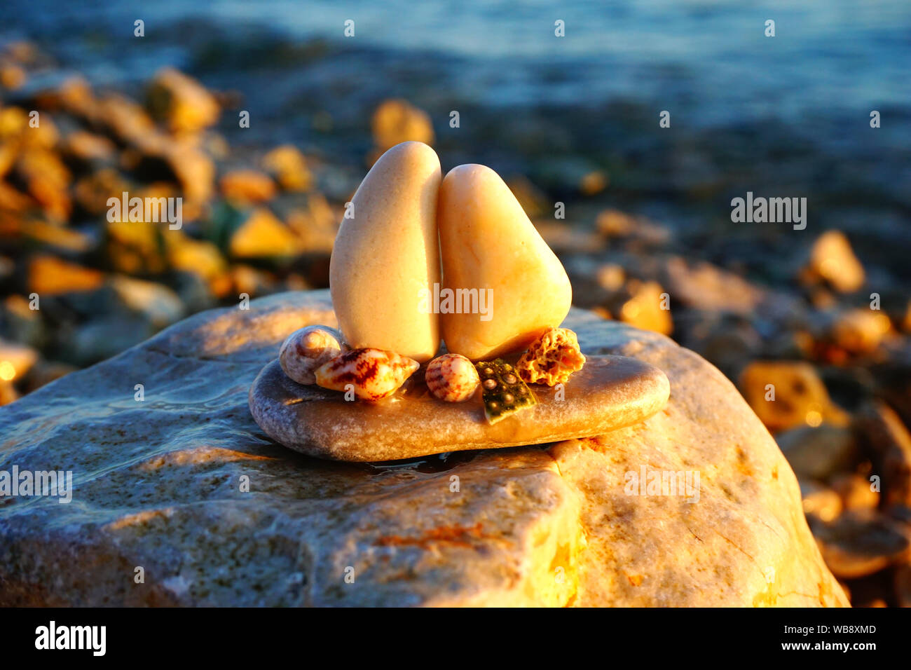 Pebble arts and nature and marine background with small boat made from pebbles and sea shells on the pebble beach at sunset Stock Photo
