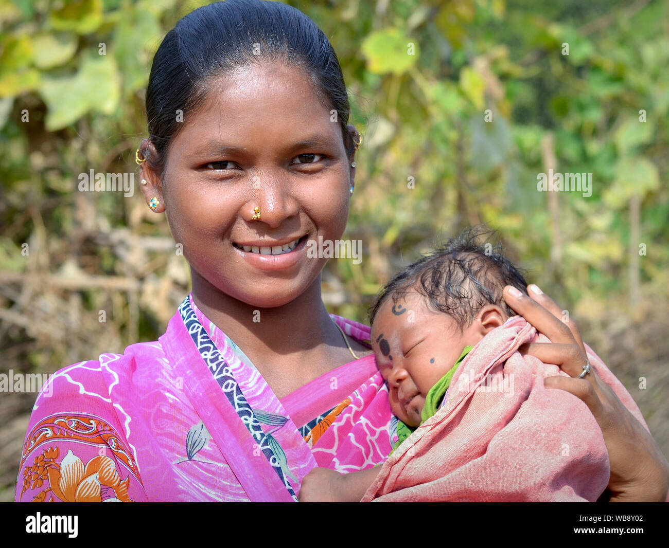 Young Indian Adivasi woman (Kuvi Kondh tribe) and her sleeping newborn baby pose for the camera. Stock Photo