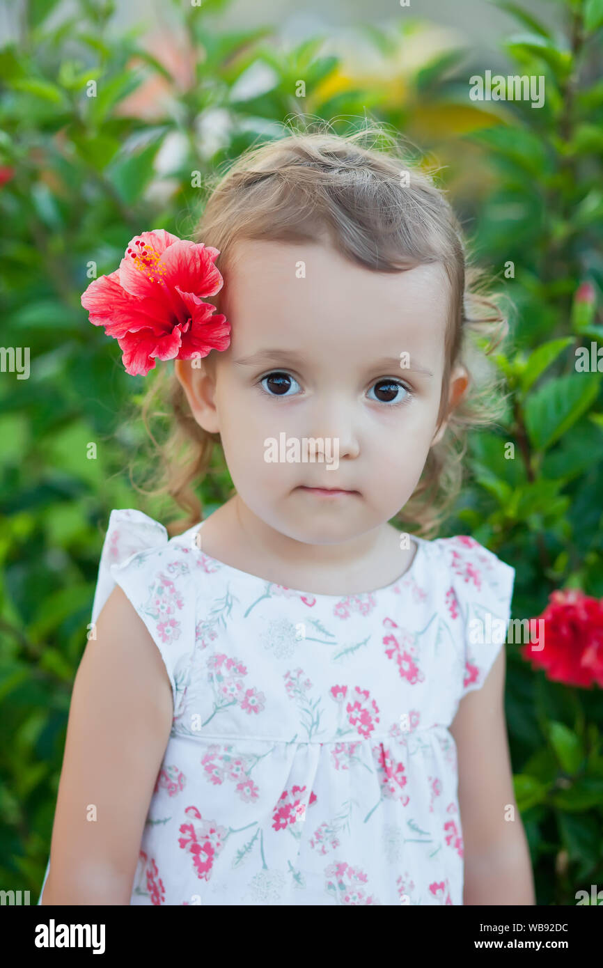 Little child girl with red flower behind her ear Stock Photo - Alamy