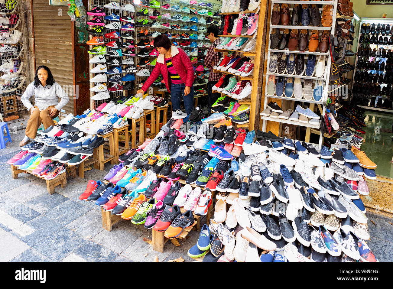 Hanoi, Vietnam - February 21, 2016: Vendors at street market selling sports  shoes and sneakers in old city of Hanoi in Southeast Asia in Vietnam. Local  business of traders and traditional shop