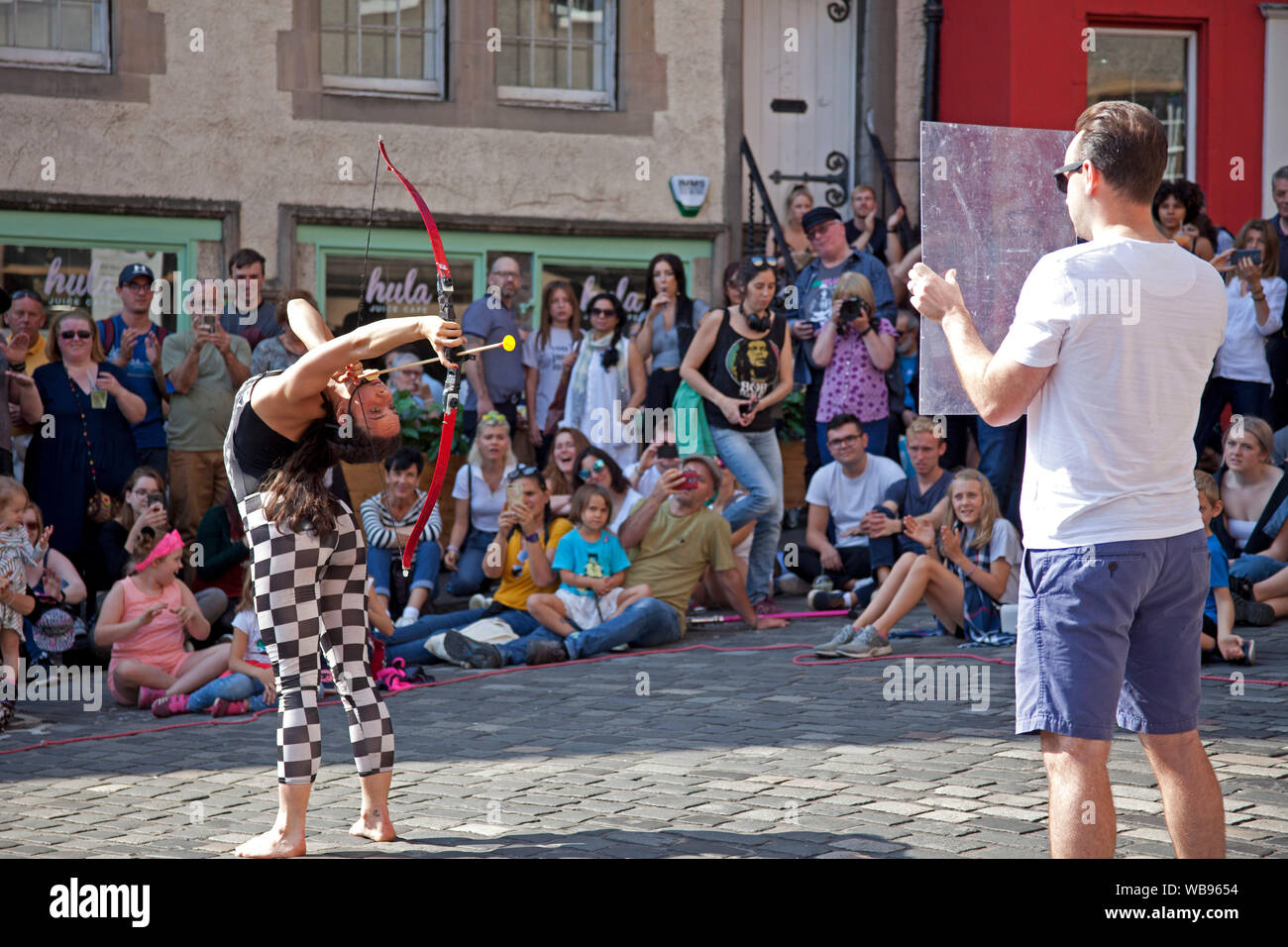 Edinburgh Fringe crowds, Grassmarket and Royal Mile, Scotland, UK. 25th August 2019. Crowds were out for the very sunny last Sunday of The 2019 Edinburgh Festival Fringe. Shannen No Bones Jones drew a crowd at foot of Victoria Street for her archery contortionist act. Stock Photo