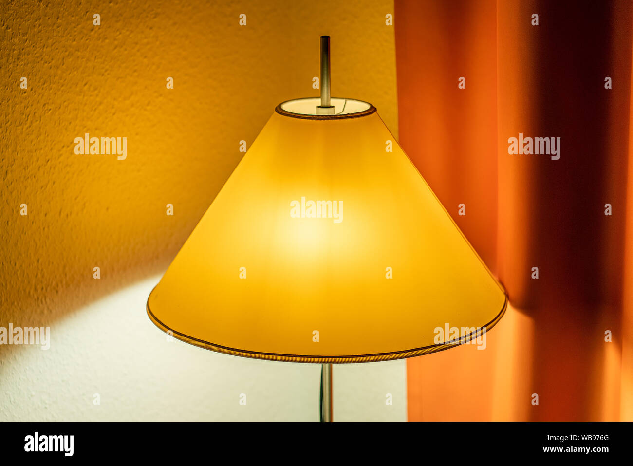 Lamp with a yellow shade and an orange curtain in the background glowing with cosy golden light Stock Photo