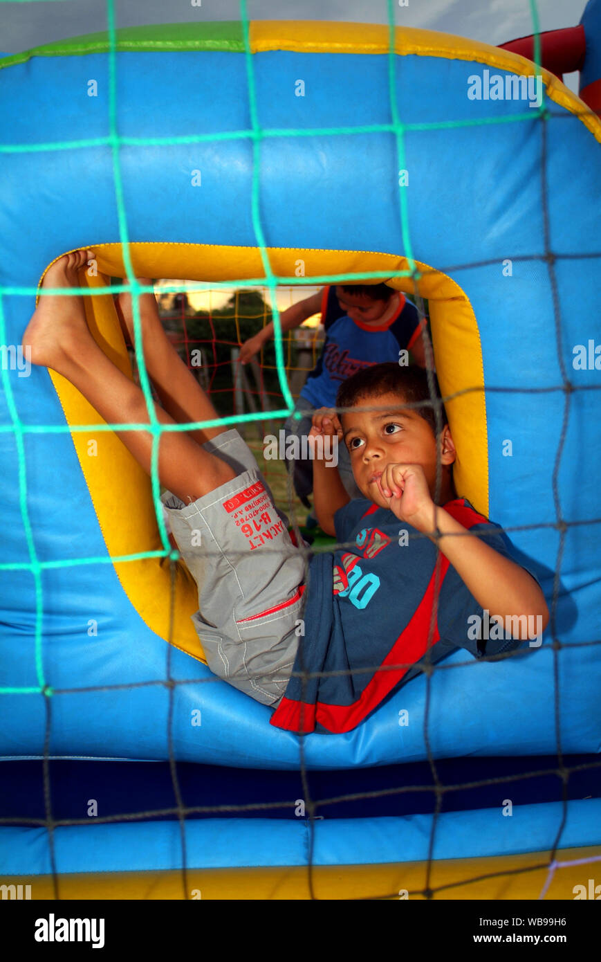 A young boy with a blue and red shirt is seating with his legs upside in the center of a light blue and yellow inflatable game, he look like dreaming Stock Photo