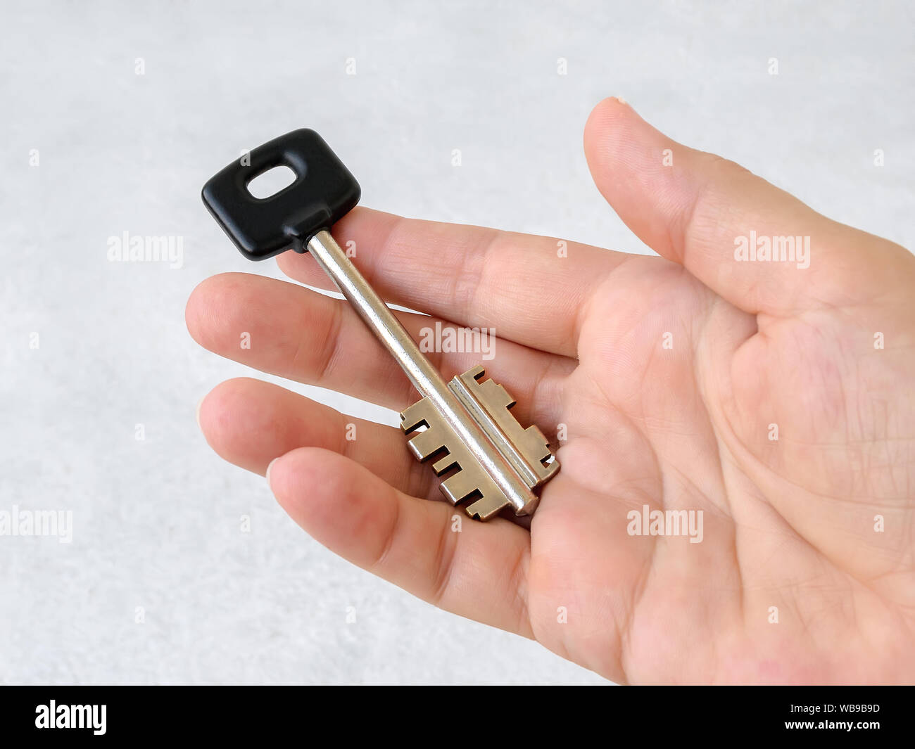 Large house key with black head lies on the open palm of a caucasian ...