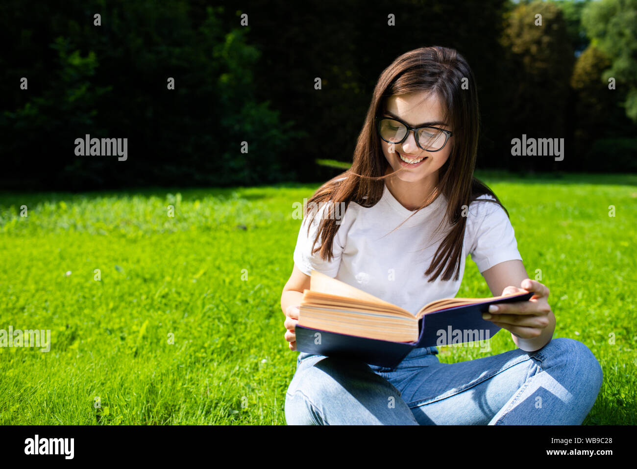 Enthusiastic student girl with book studying in campus park Stock Photo