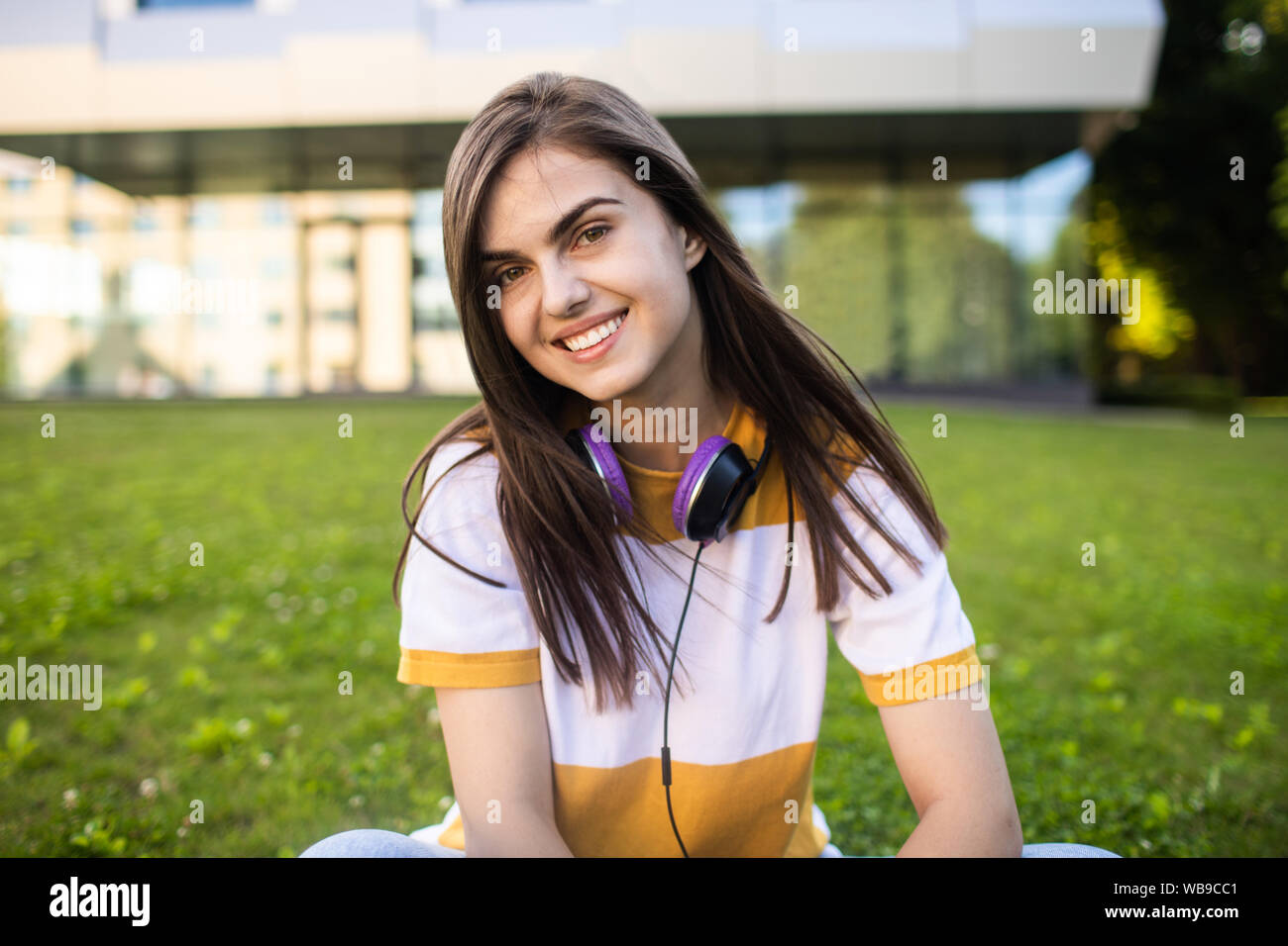 Portrait of smiling cute college girl with headphones posing in front of her alma mater Stock Photo
