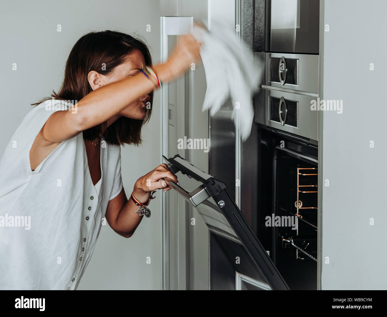 Blonde woman with green eyes in modern kitchen checks the oven because