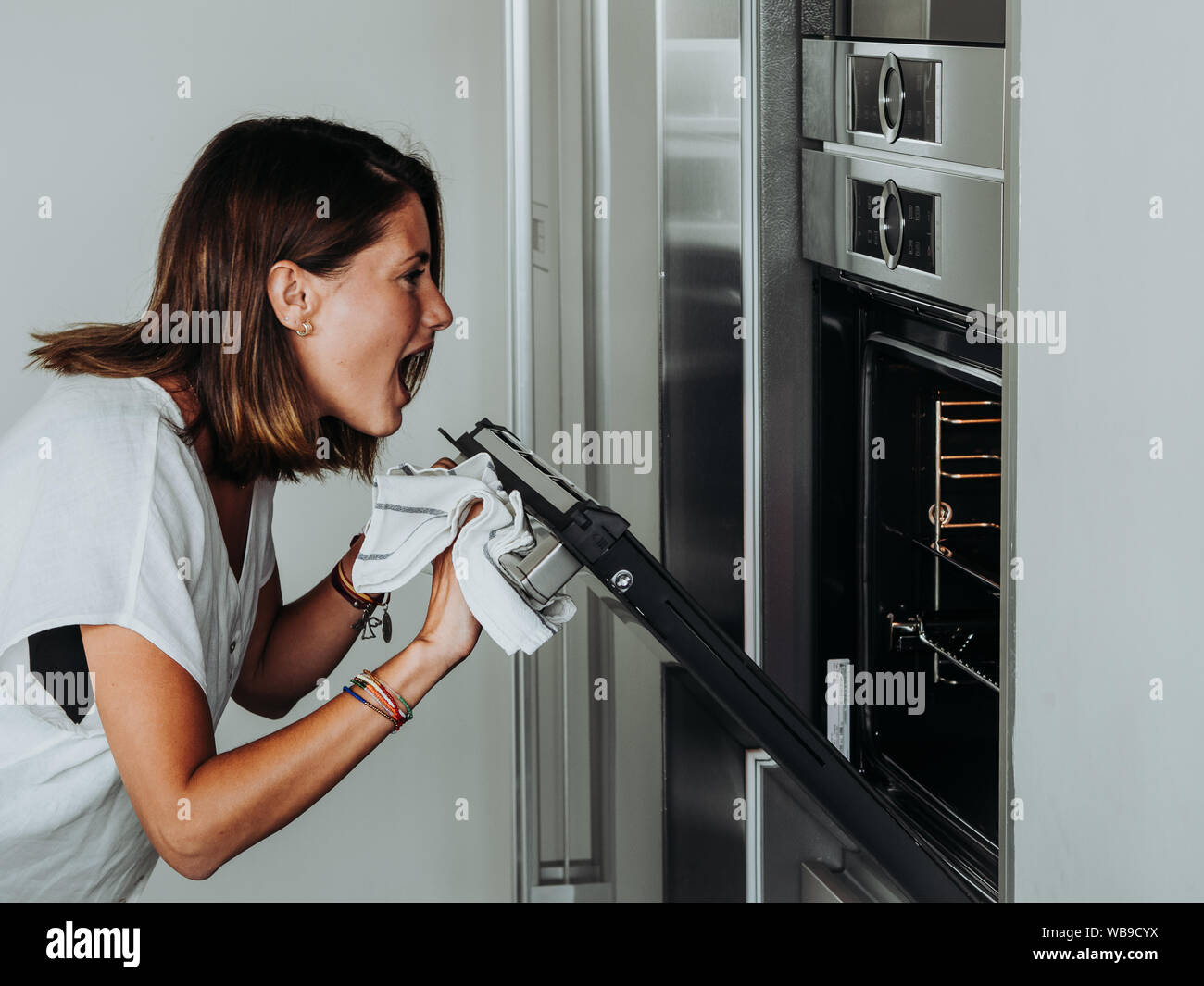 Blonde woman with green eyes in modern kitchen checks the oven because