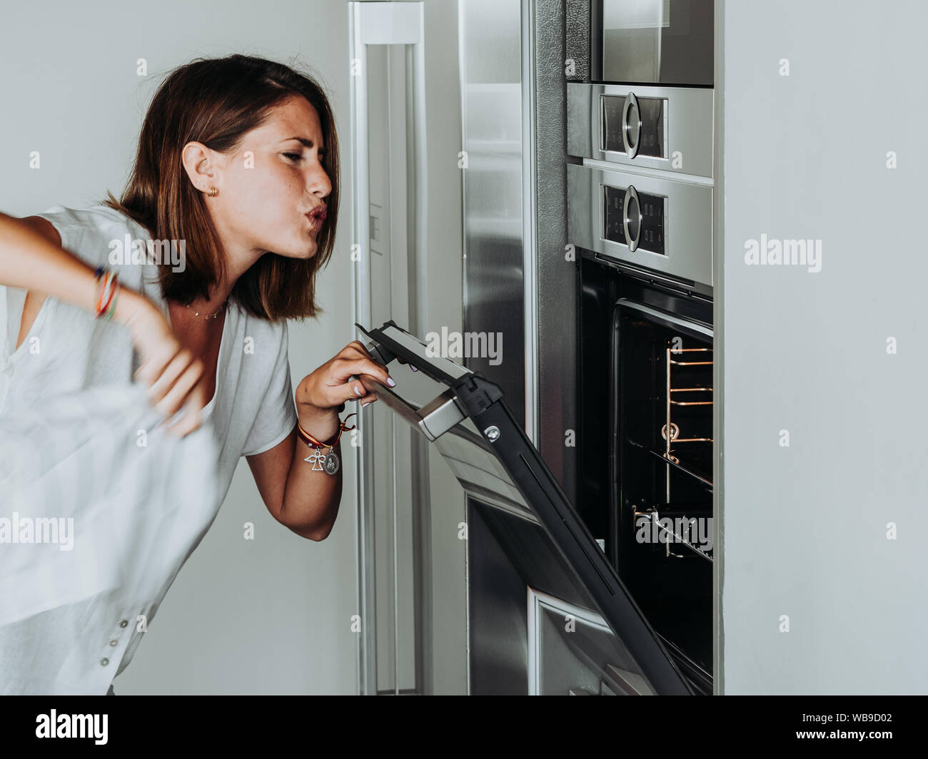 Blonde woman with green eyes in modern kitchen checks the oven because