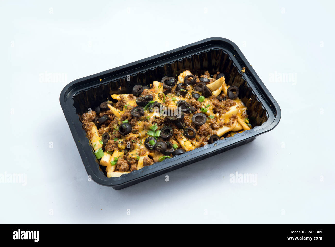 A high contrast Hero shot of a Take-Away Hot Loaded fries / chips with ground meat, olives, cheese, jalapeno, sauce & oregano, on a minimal white back Stock Photo