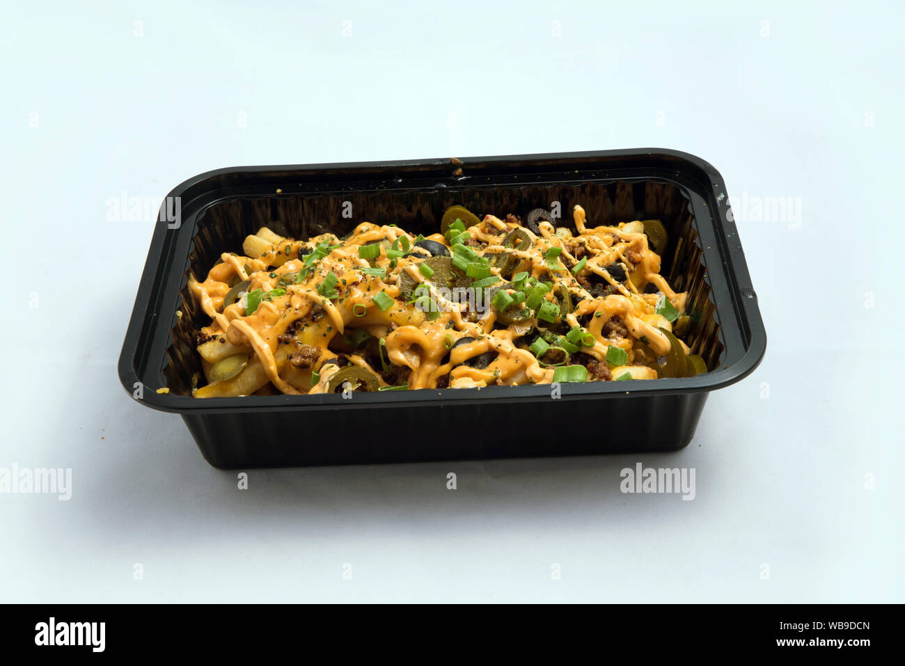 A high contrast Hero shot of a Take-Away Hot Loaded fries / chips with cheese, ground meat, olives, jalapeno, sauce & oregano, on a minimal white back Stock Photo