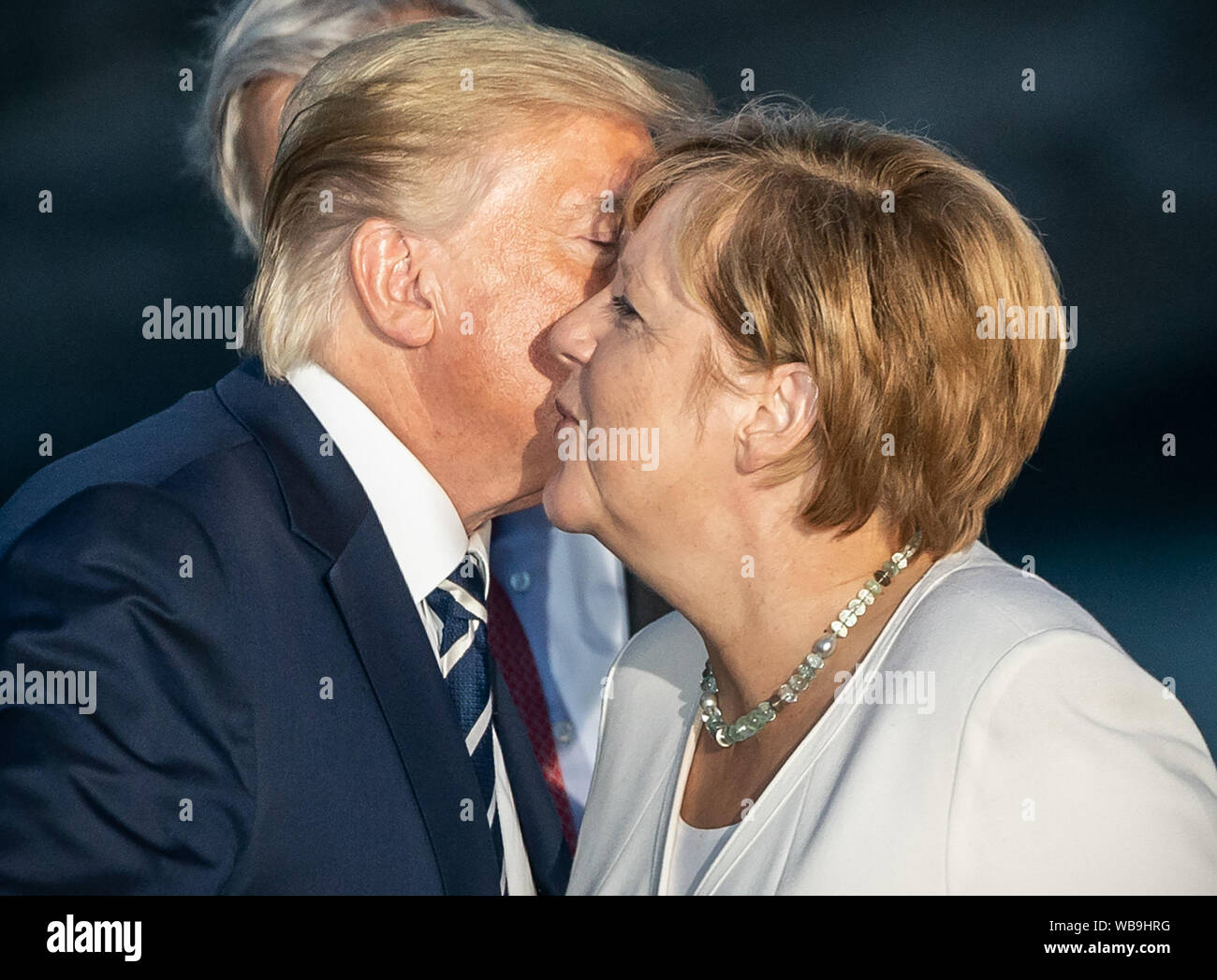 Biarritz, France. 25th Aug 2019. Donald Trump, President of the USA, kisses  German Chancellor Angela Merkel (CDU) to greet her at a joint family photo  at the G7 summit. The G7 summit