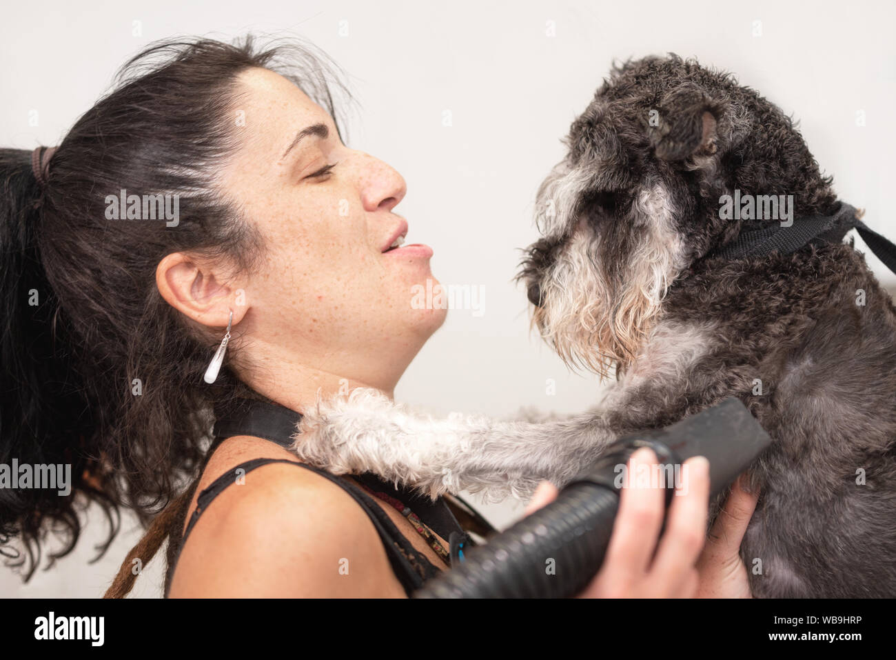 Female pet groomer hugging tenderly a schnauzer dog in grooming salon. Pet love and care concept