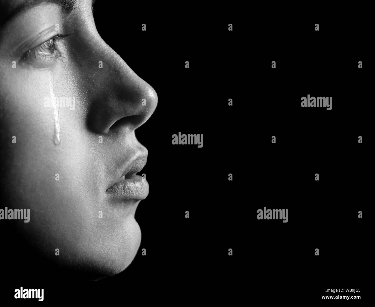 sad woman crying, looking aside on black background with copy space, closeup portrait, profile view, monochrome Stock Photo