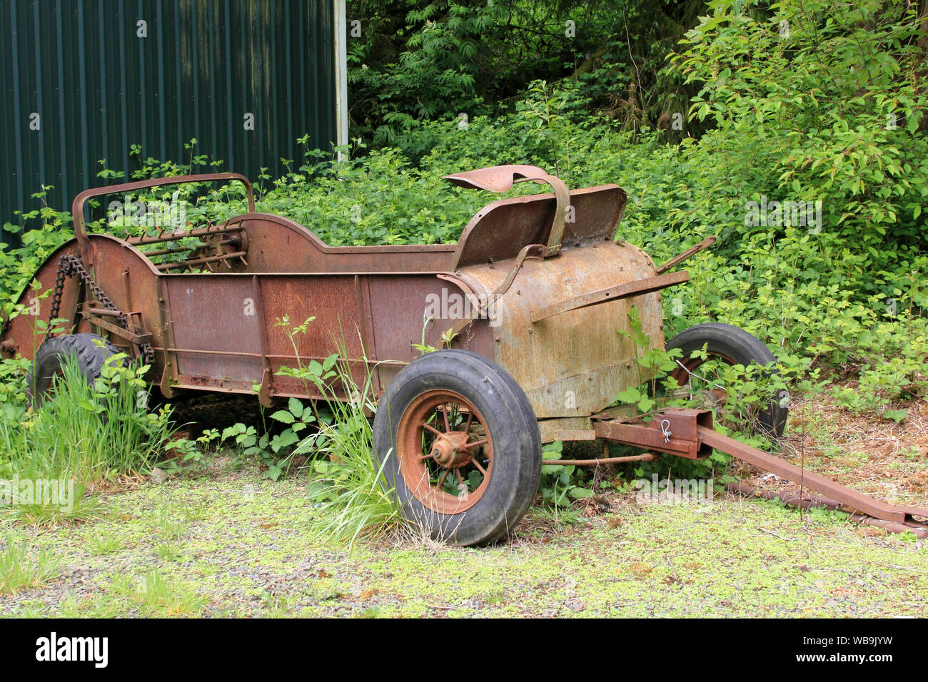 An ancient Manure spreader is left among the weeds to rust Stock Photo