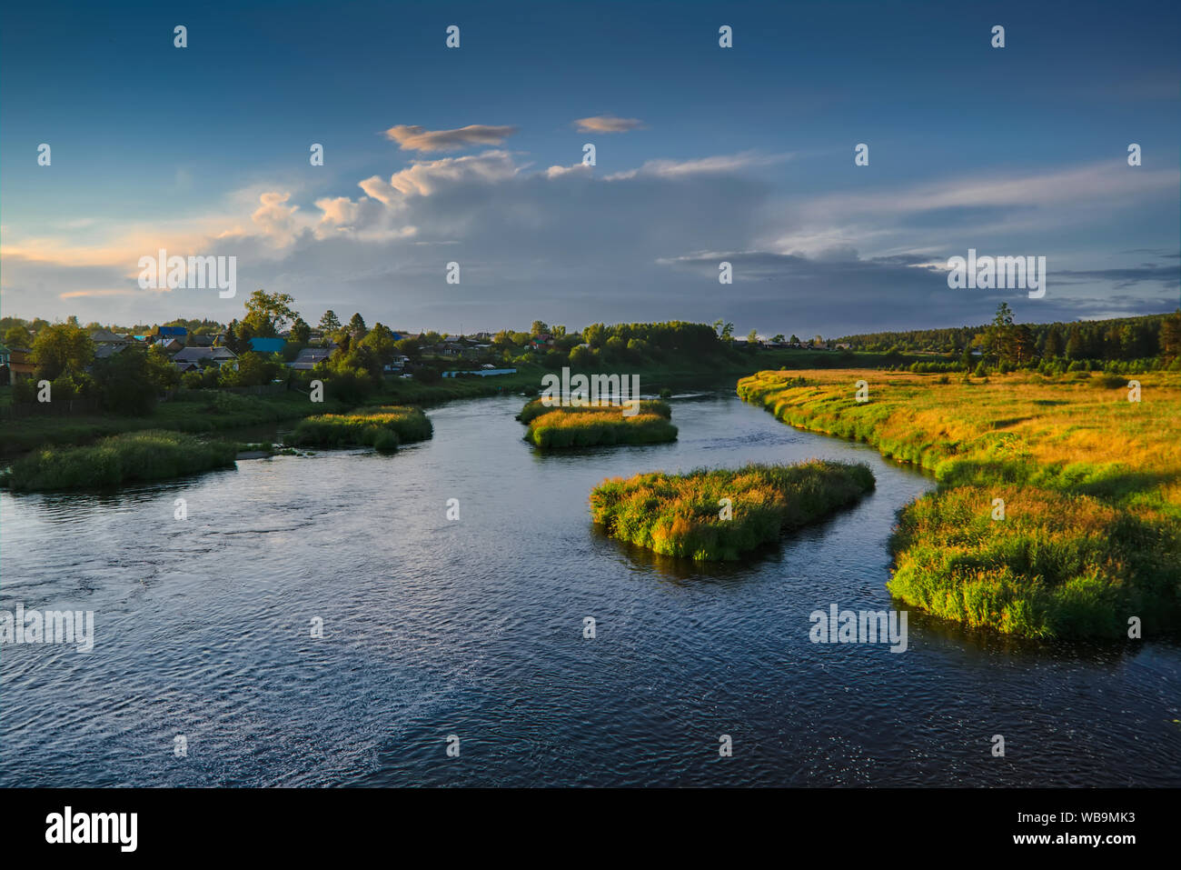 The Russian village on the banks of the river against the backdrop of the setting sun. Stock Photo