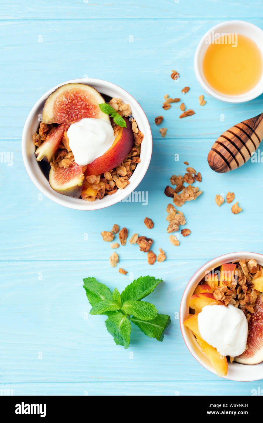 Granola with figs, peach and yogurt in bowl on blue wooden table background. Top view. Concept of healthy eating, dieting, well being Stock Photo