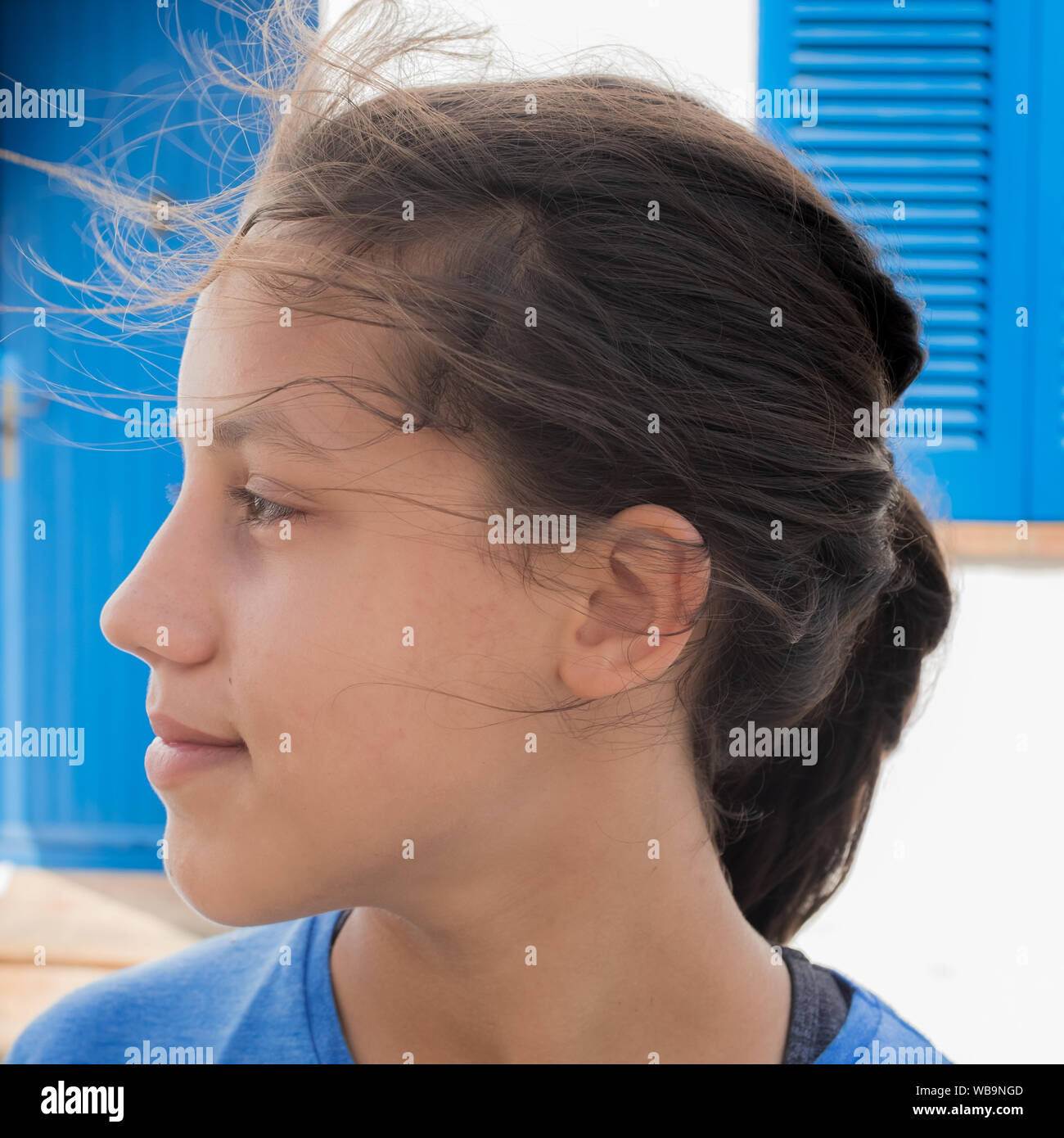 Close up profile of a cheerful young girl looking away with hair blowing in wind outdoors. Innocence and happiness concepts. Stock Photo