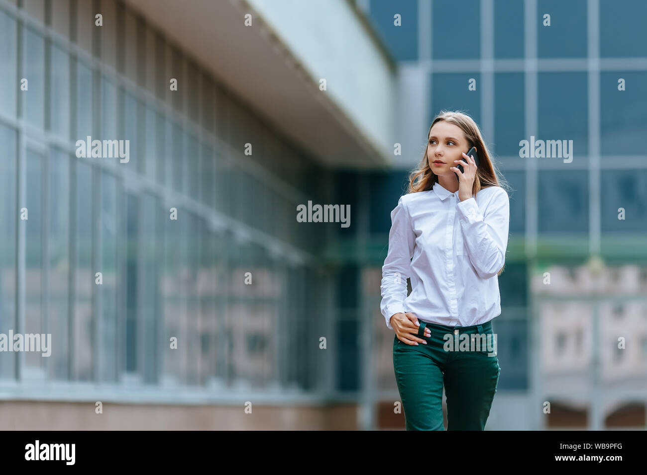 Young famale calling on a smartphone and walking on street. Attractive businesswoman talking by phone. Office building and in the Business District Stock Photo