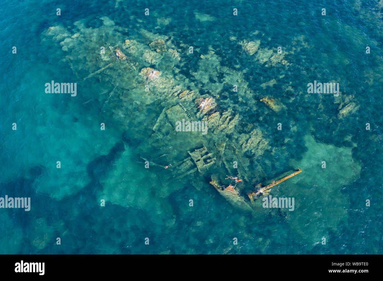 View from above, stunning aerial view of a wreck inside the Marine Protected Area of Tavolara. Some people snorkel in an emerald green sea. Stock Photo