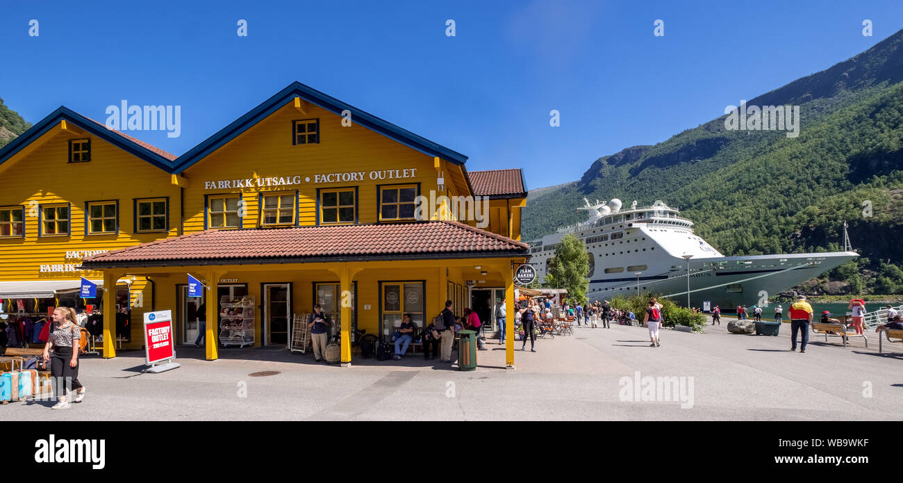 Tourists in Flåm, FABRIK KUTSALG FACTORY OUTLET, shops, yellow wooden house, excursion ship, fjord, mountain, trees, blue sky, Sogn og Fjordane, Norwa Stock Photo
