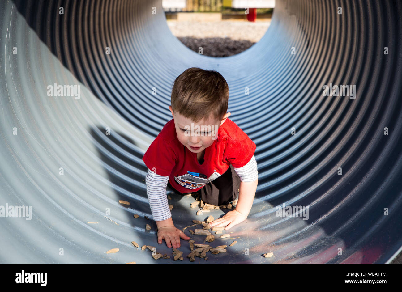 A little boy crawls through a playground tunnel, exploring and having fun Stock Photo