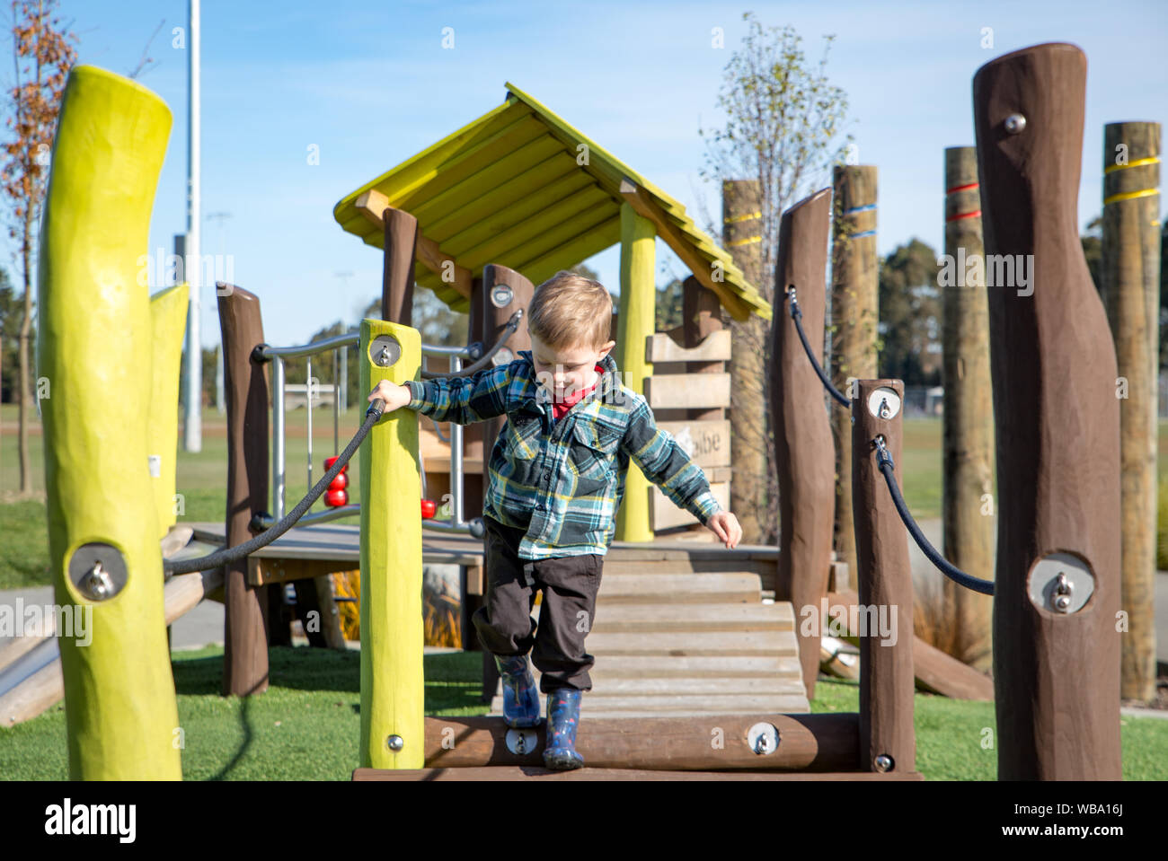 A little boy carefully practices walking across the swing bridge on the playground fort Stock Photo