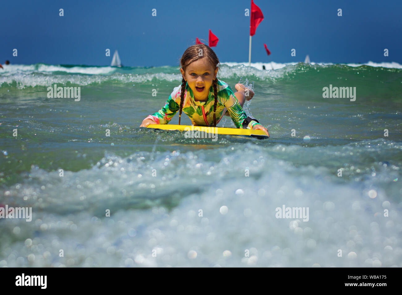 Happy baby girl - young surfer ride on surfboard with fun on sea waves. Active family lifestyle Stock Photo