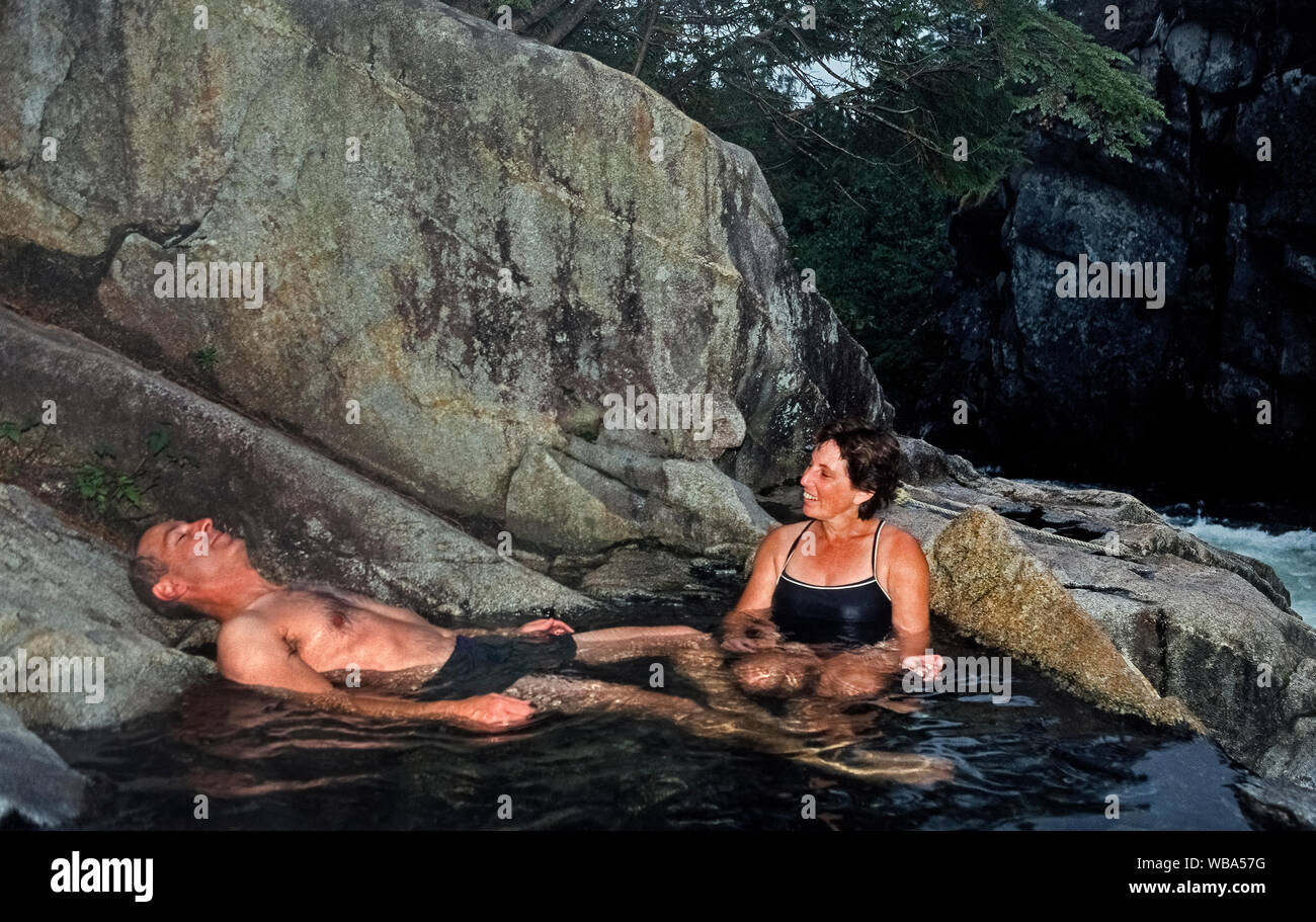 An adult couple relaxes in one of nine separate hot springs that are part of Baranof Warm Springs, an isolated tourist destination on Baranof Island in the Alexander Archipelago along the panhandle of southeast Alaska, USA. Located on same island as the Inside Passage community of Sitka, access to these soothing waters is only by private or tour boats and floatplanes. Temperature of these natural hot springs ranges from lukewarm to 120 degrees Fahrenheit (49 Celsius). Stock Photo