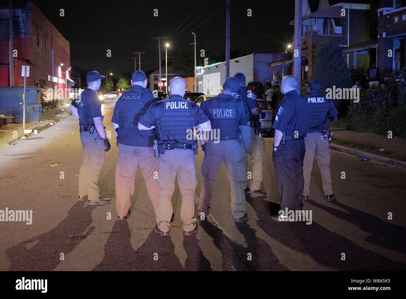 Group of Detroit police Special Ops officers stand in a street, trying