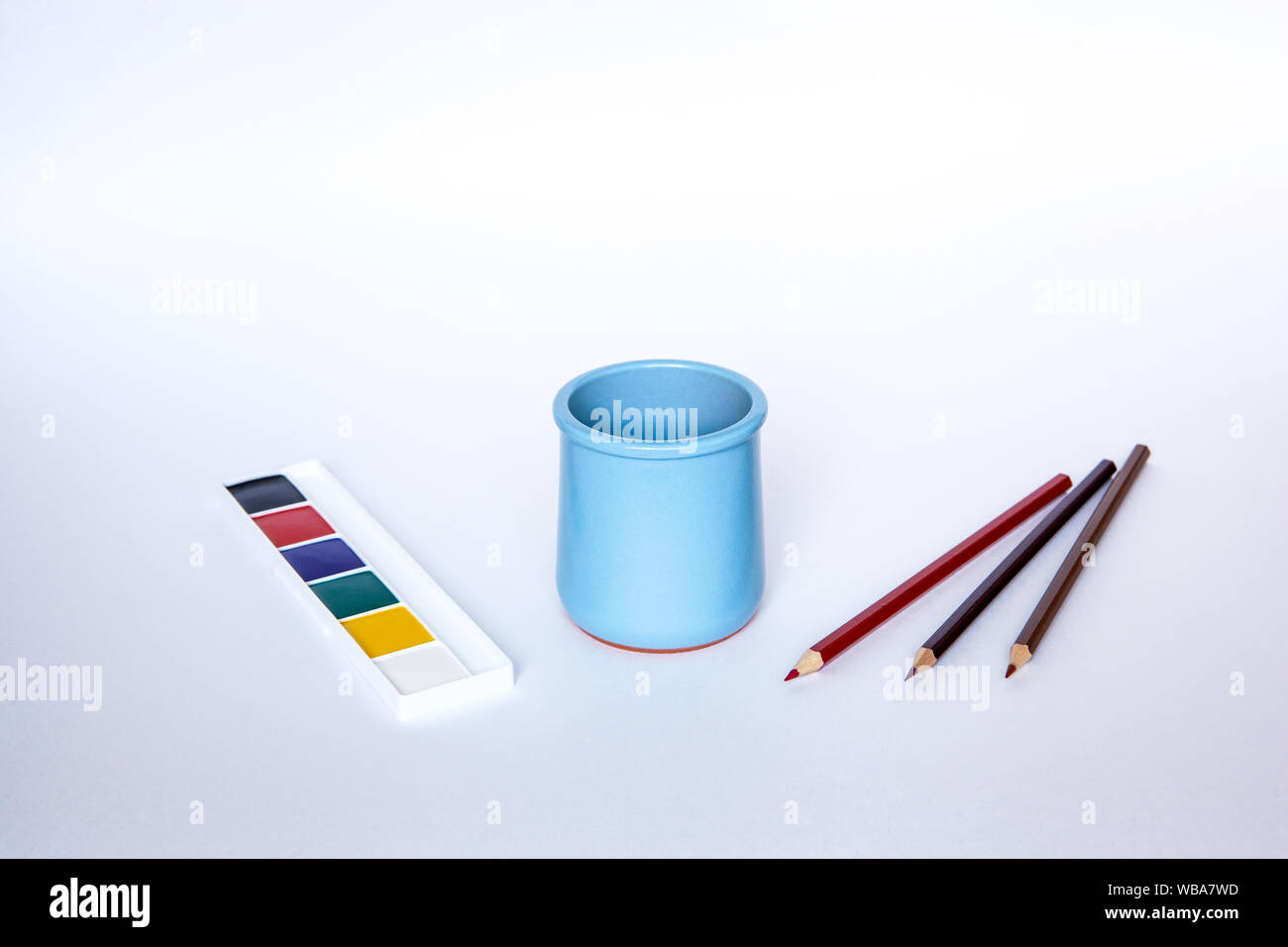 Blue vase for pencils on the white background with various pencils and paints Stock Photo