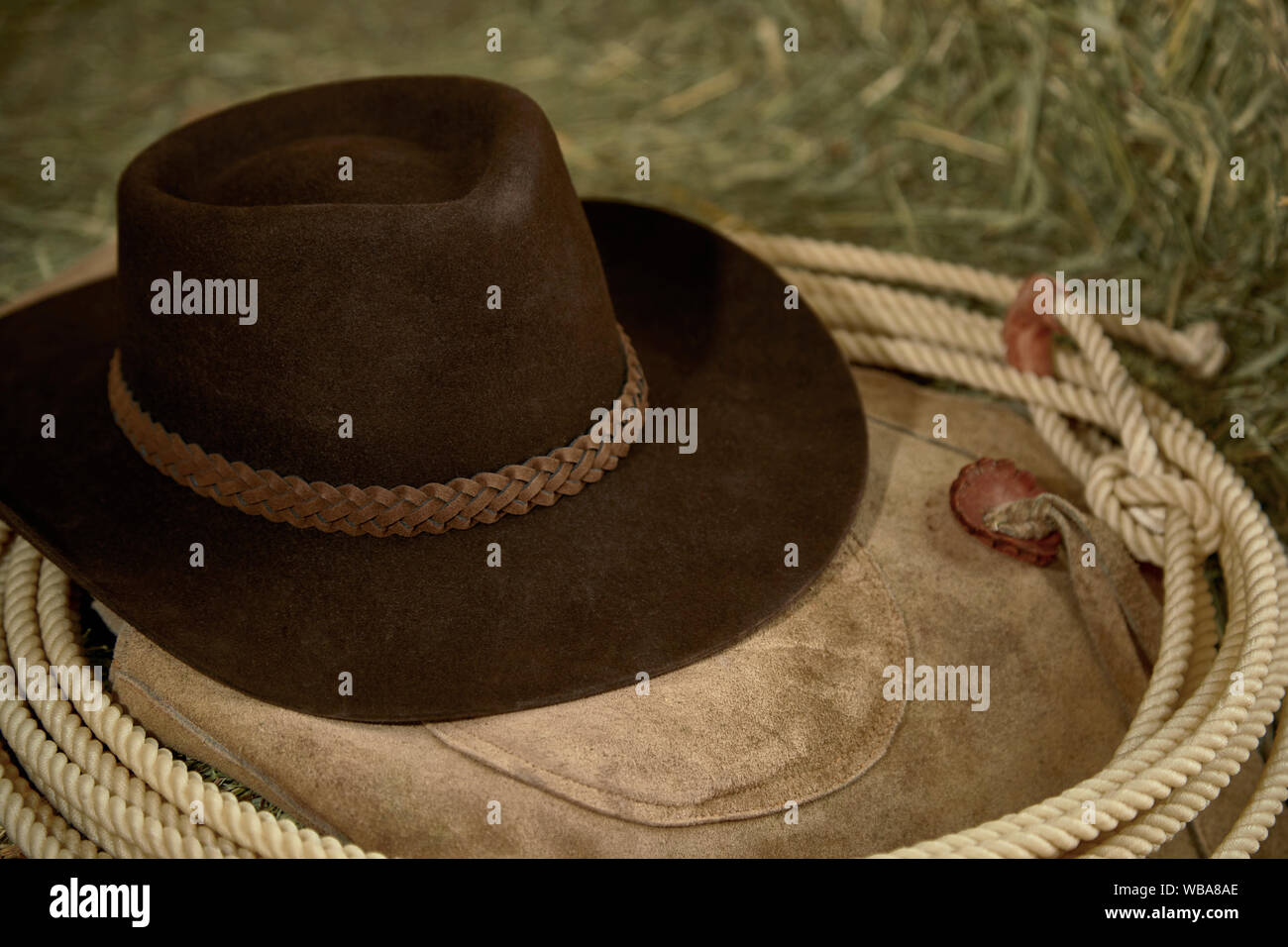 Western Cowboy hat with leather chaps and a roper's rope on hay in a barn Stock Photo