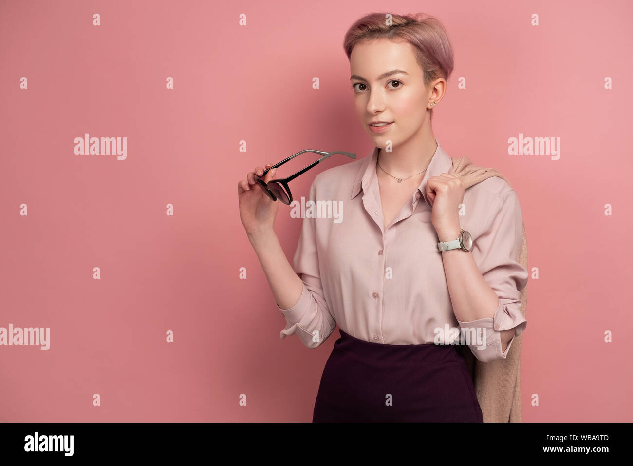 A Girl With Short Hair In A Blouse And Skirt Looks At The Camera