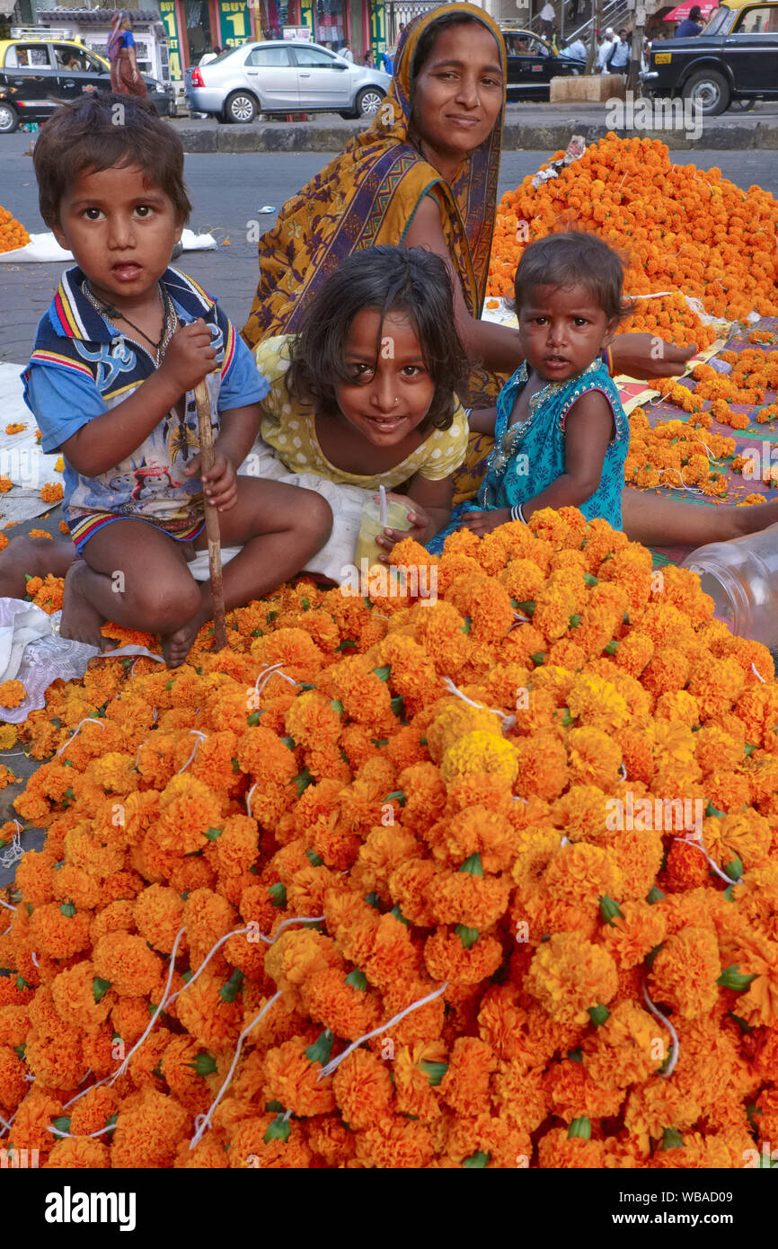 A woman migrant from West Bengal & her children squatting in a street in Mumbai, India, making garlands of marigold flowers to sell to temple visitors Stock Photo