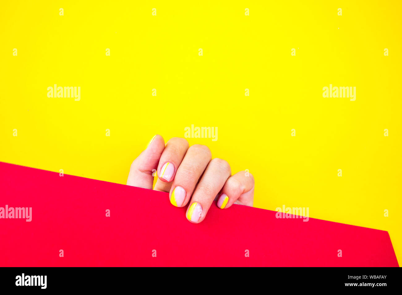 Young woman's hand with beautiful manicure on bright yellow background holding red color paper. Stock Photo