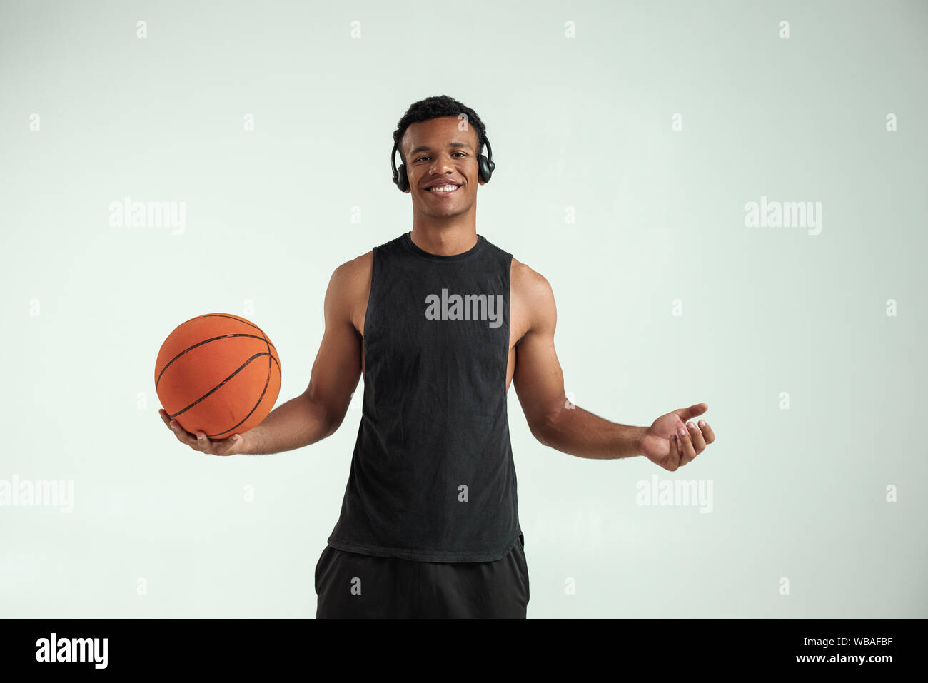 My favourite game. Cheerful young african man in headphones holding  basketball ball and listening music while standing against grey background.  Professional sport. Music concept Stock Photo - Alamy