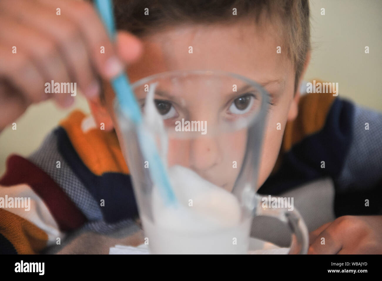 funny cute little boy in sweater watching through transparent glass holding straw sitting