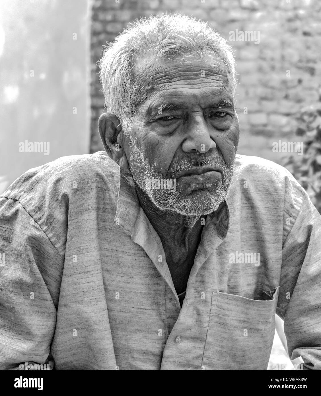 Black and White photo of Superannuated Senior Citizen in his early 80s, with wrinkle on face and neck, thinking deeply & posing with gloomy expression Stock Photo