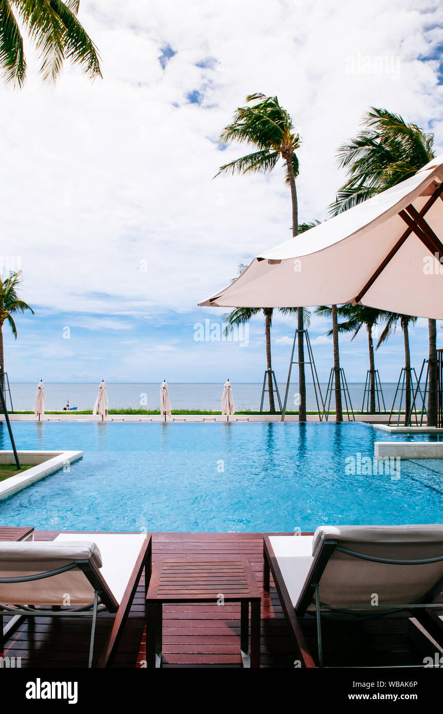 AUG 6, 2014 Hua Hin, Thailand - Tropical seaside resort style infinity edge pool with beach bed under white umbrella and coconut trees in summer Stock Photo
