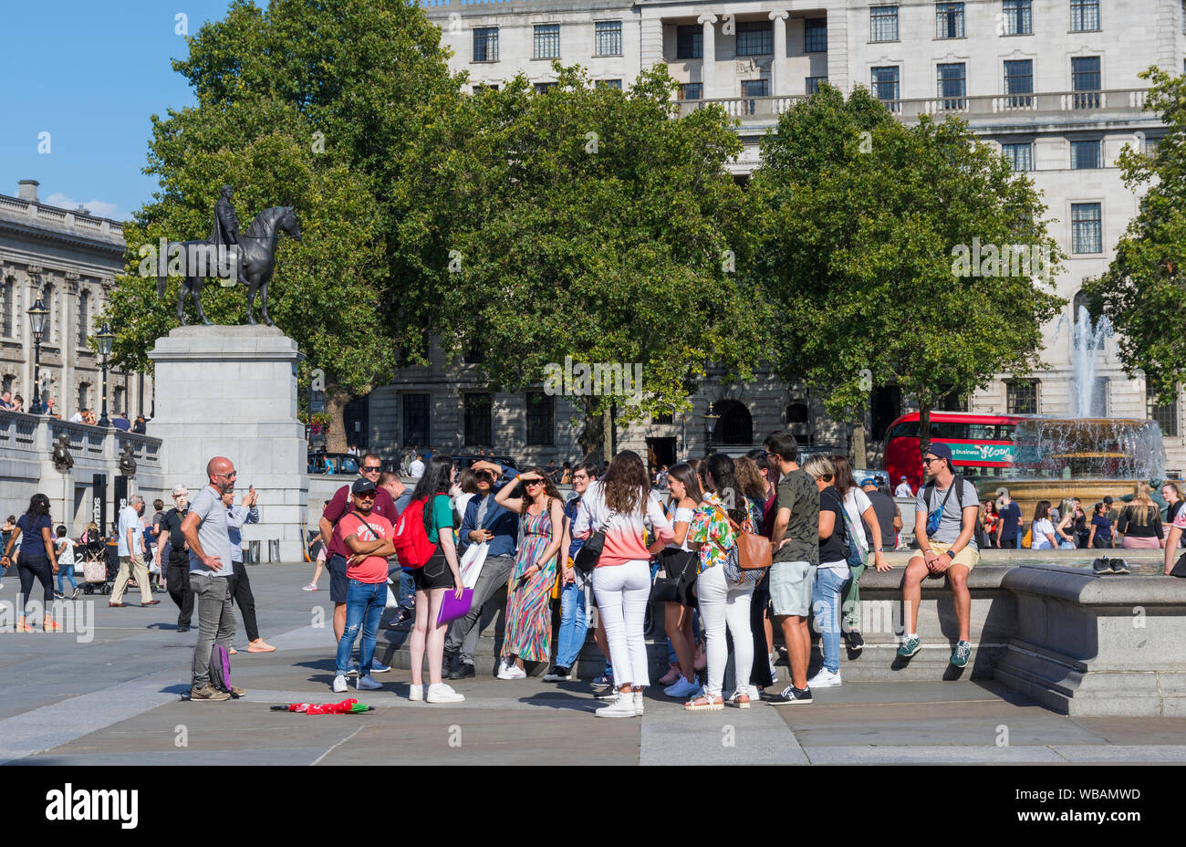 Group of tourists on a guided tour in Summer in Trafalgar Square, Charing Cross, Westminster, Central London, England, UK. Stock Photo